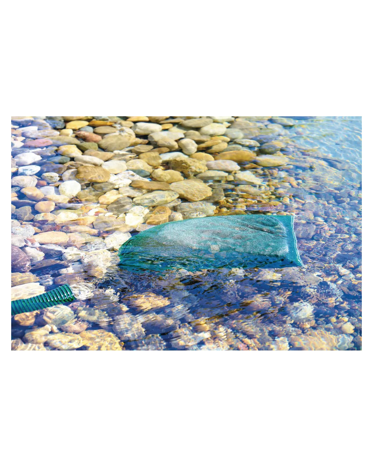 Netzbeutel mit AquaHumin-Torf liegt im flachen Wasser auf Kieseln