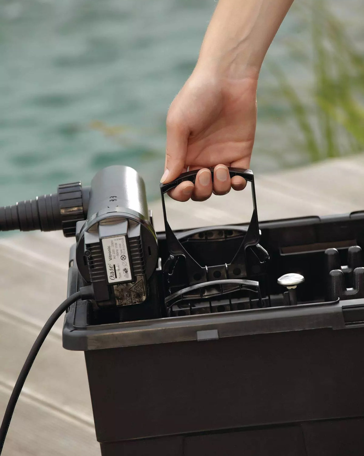 Geöffneter Filter des OASE BioSmart Set 14000 am Teich: Hand am Reinigungsgriff, links der UVC-Klärer