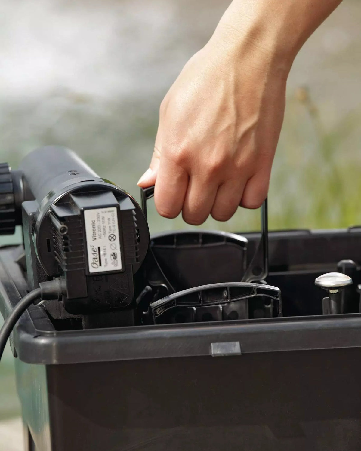 Geöffneter BioSmart-Filter mit UVC-Klärer am Teich, eine Hand zieht den Reinigungsgriff