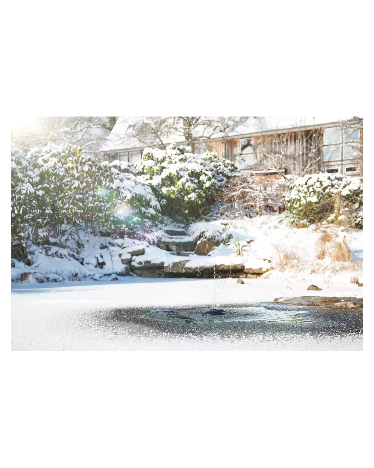 OASE IceFree 4 Seasons im verschneiten Gartenteich: offene Stelle am Schwimmkörper mit kleiner Fontäne