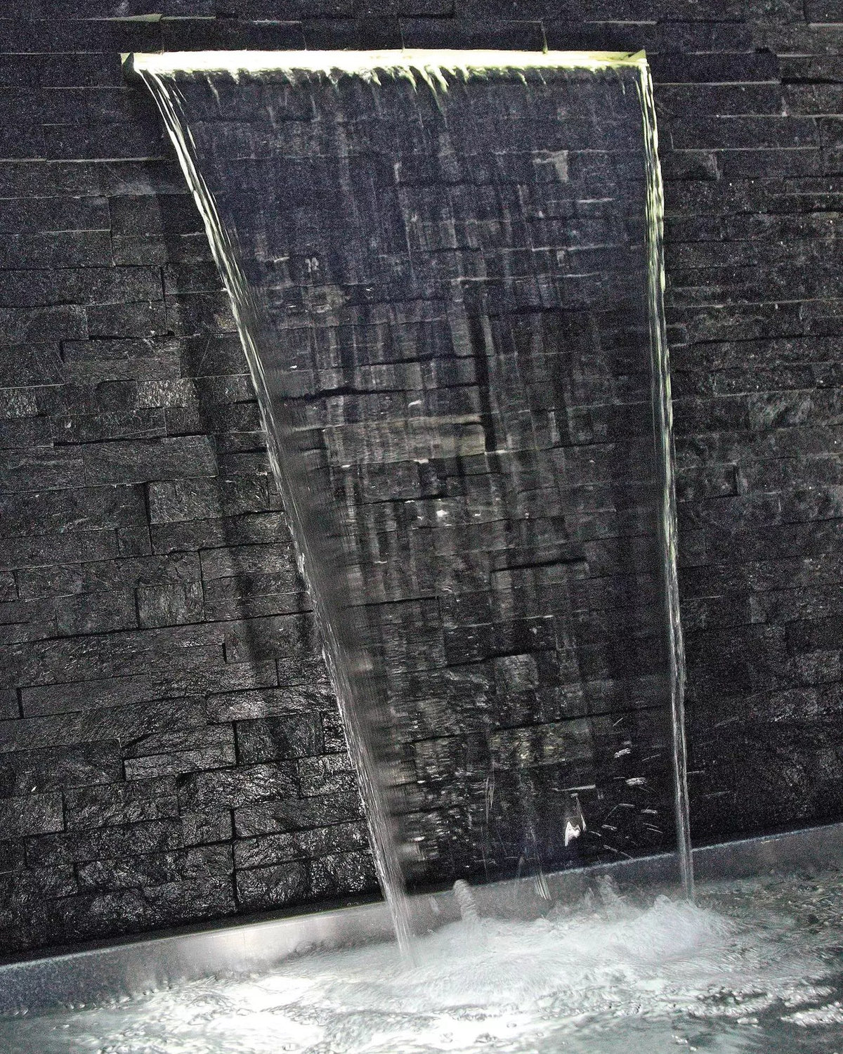 Wandwasserfall an dunkler Natursteinwand mit Waterfall Illumination