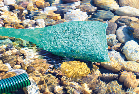 Aktivkohle im Netzbeutel zur Wasserreinigung im Teich zwischen Steinen im Wasser
