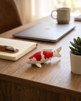 Kohaku Koi-Figur als besondere Japan-Deko auf dem Schreibtisch neben Laptop und Pflanze.