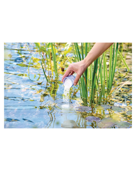 Weißes OptiPond-Pulver wird aus dem Messbecher ins Teichwasser gegeben