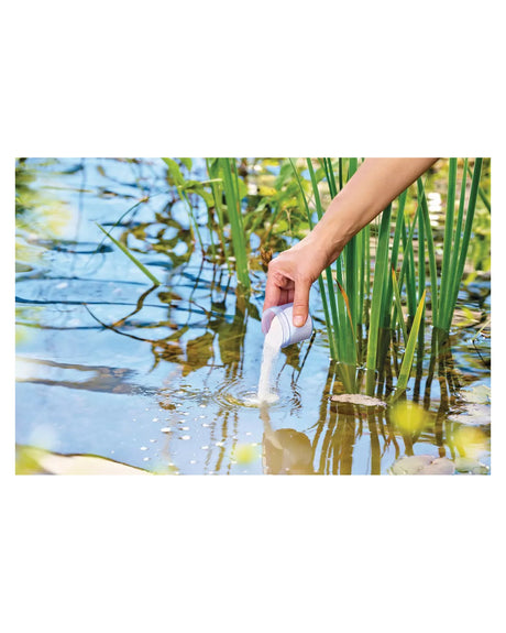 OxyPlus-Granulat wird aus einem Messbecher ins Teichwasser gegeben