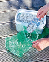 PondLith-Zeolith wird mit einer Schaufel aus der Box in einen grünen Netzbeutel gefüllt