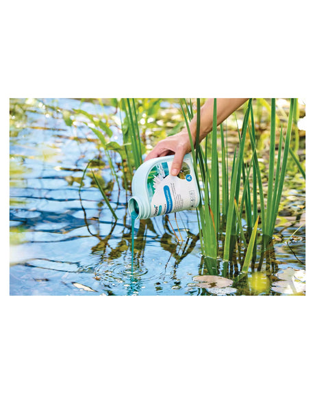 Blaue Safe&Care-Flüssigkeit wird aus der Flasche zwischen Schilf in den Teich gegossen