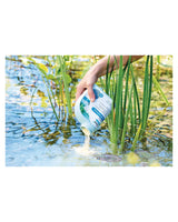 SediFree-Granulat wird aus der Flasche zwischen Schilf ins Teichwasser gegeben
