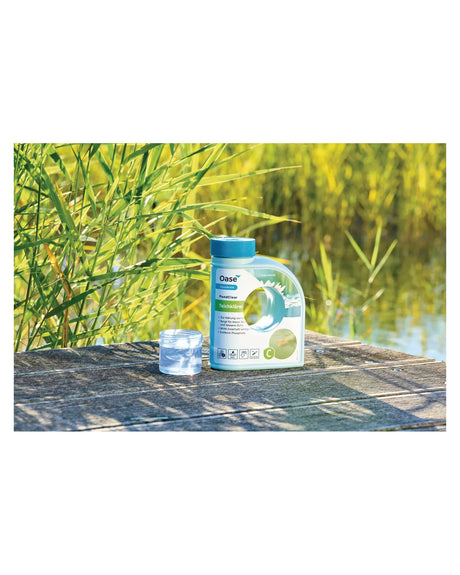 PondClear 500 ml mit Messbecher auf einem Holzsteg vor Schilf