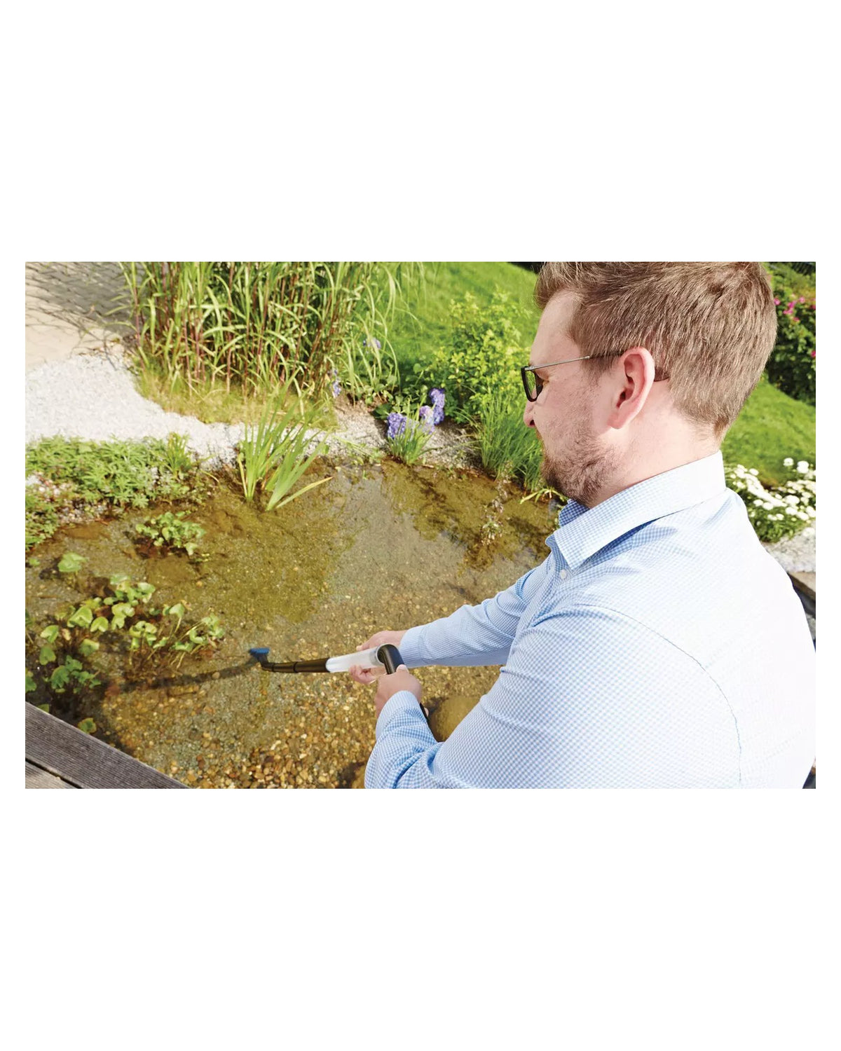 Mann saugt mit dem Saugrohr des OASE PondoVac Classic die Flachwasserzone eines Gartenteichs ab