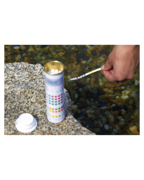Offene Dose der OASE QuickSticks 6in1 auf einem Stein am Wasser, daneben Deckel und Teststreifen